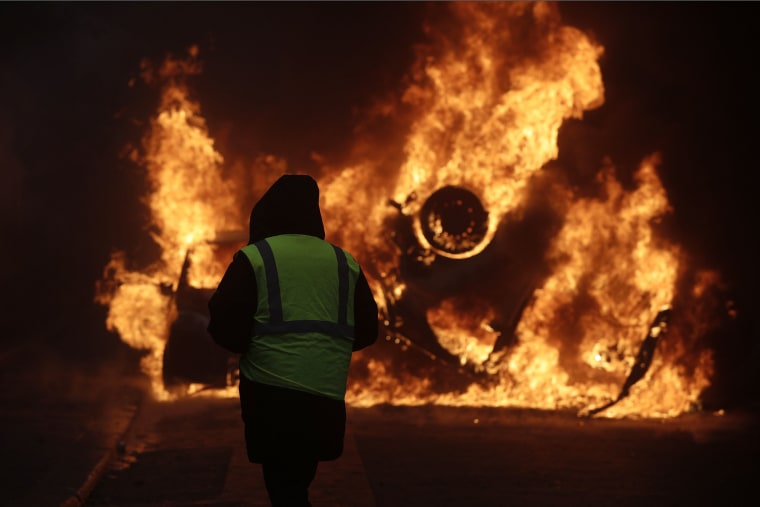 Image: A protester watches a burning car near the Champs-Elysees in Paris