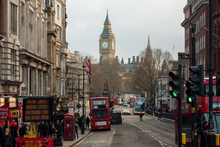 Image: Buses pass through traffic lights near the Houses of Parliament in London