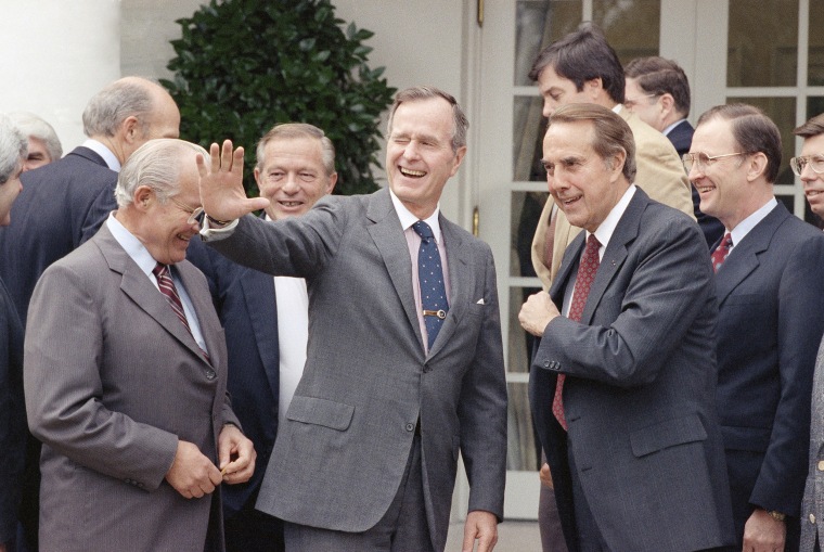 President George H.W. Bush winks as he ends a session on Oct. 25, 1990, in the White House Rose Garden at Washington, with Republican members of Congress, including Senate Minority Leader Bob Dole of Kansas.