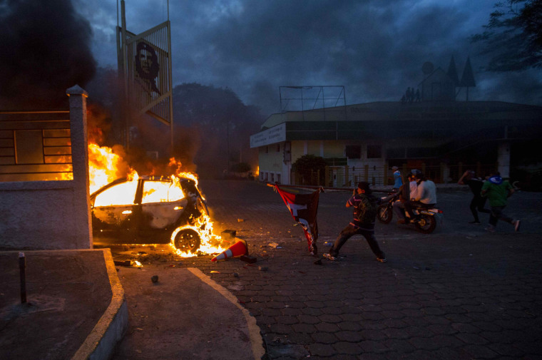 Image: A man throws a ruling party flag at a burning vehicle during protests in Managua, Nicaragua, on May 30, 2018.