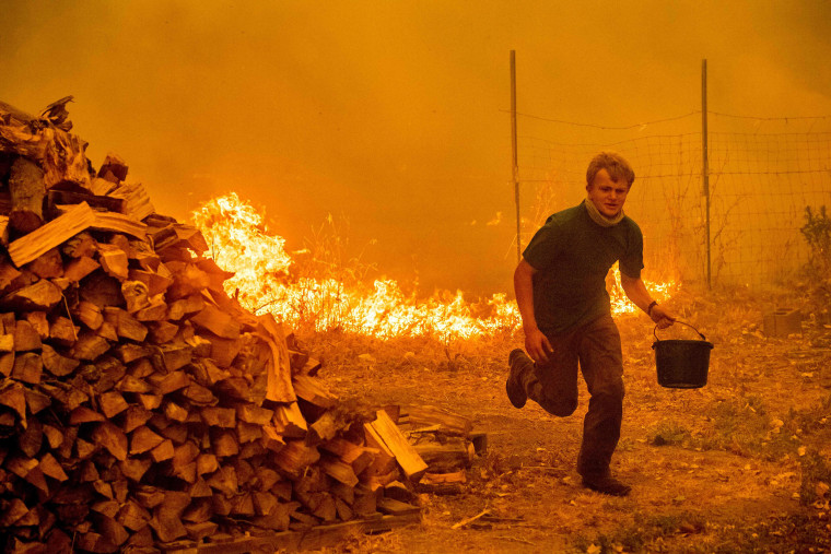 Image: Alex Schenck carries a water bucket while fighting to save his home from the Ranch Fire