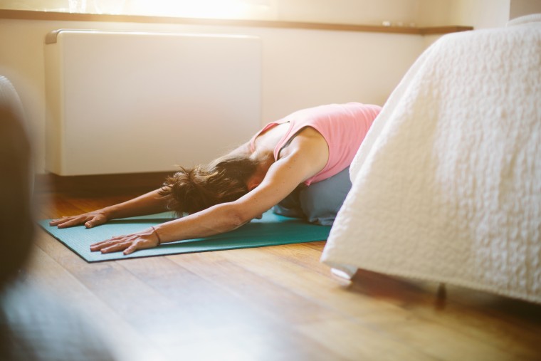 image: Mid adult woman in yoga position on bedroom floor