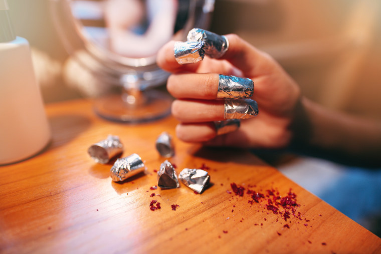 Closeup shot of a woman using a foil to give a nail manicure. Woman remove a cuticle nail with foil. Shallow depth of field with focus on foil.