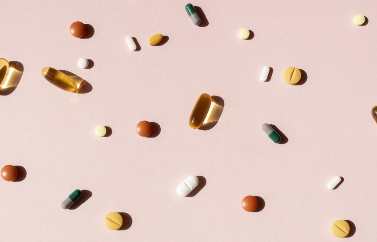 Top view of various pills and tablets on the pink background
