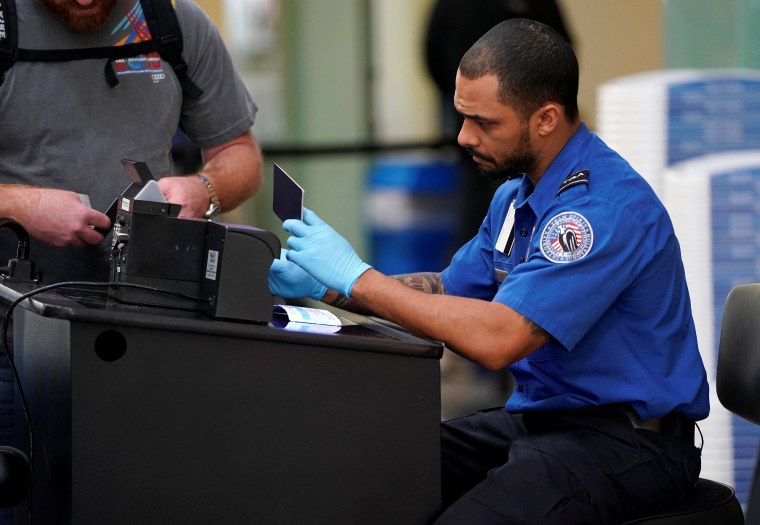 Image: An employee with the Transportation Security Administration (TSA) checks the documents of a traveler at Reagan National Airport in Washington