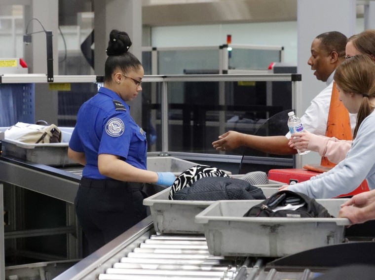 Image: A Transportation Security Administration employee helps air travelers submit their bags for inspection at Hartsfield Jackson Atlanta International Airport