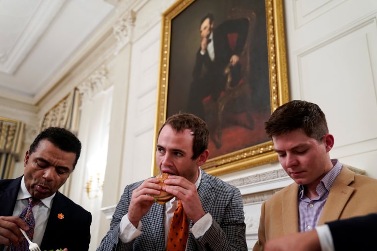 Image: Clemson wide receiver Hunter Renfrow (C) eats a fast food hamburger as the 2018 College Football Playoff National Champion Clemson Tigers are welcomed in the State Dining Room of the White House due to the partial government shutdown in Washington