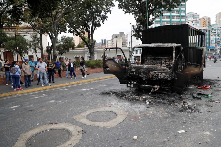 Image: People look at a burned truck in a street after a protest in Caracas