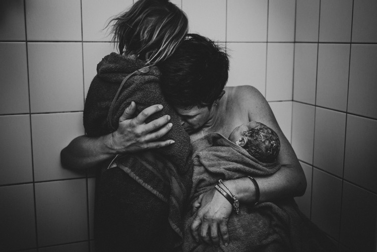 After labor a mom holds two of her children wrapped in towels. This image won second place for black and white photography.