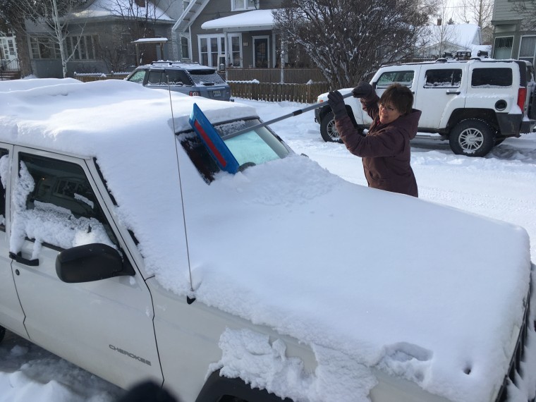 Becky Jackson using the SnoBrum to clean off a Jeep in Montana.