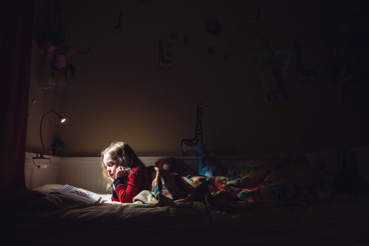 Image: A six year old girl is reading in her bed at night.