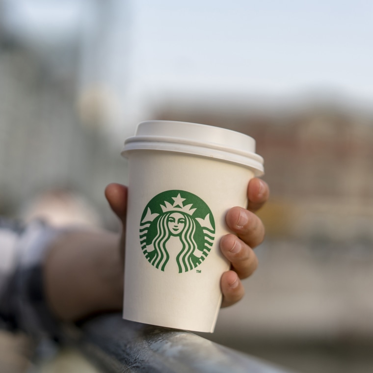 A girl holds a Starbucks coffee cup on a bridge.  Starbucks