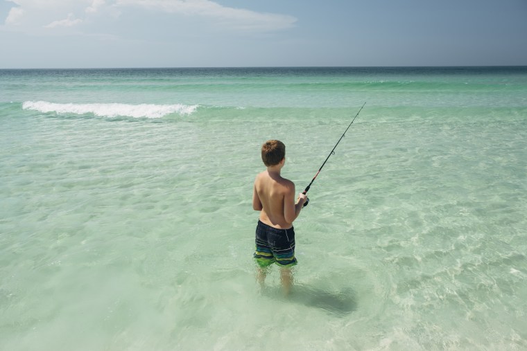 Rear view of shirtless boy fishing in sea