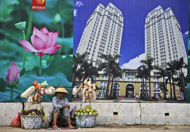 A snack and fruit vendor waits for customers near the advertisement board of a shopping mall and apartment building in Ho Chi Minh City