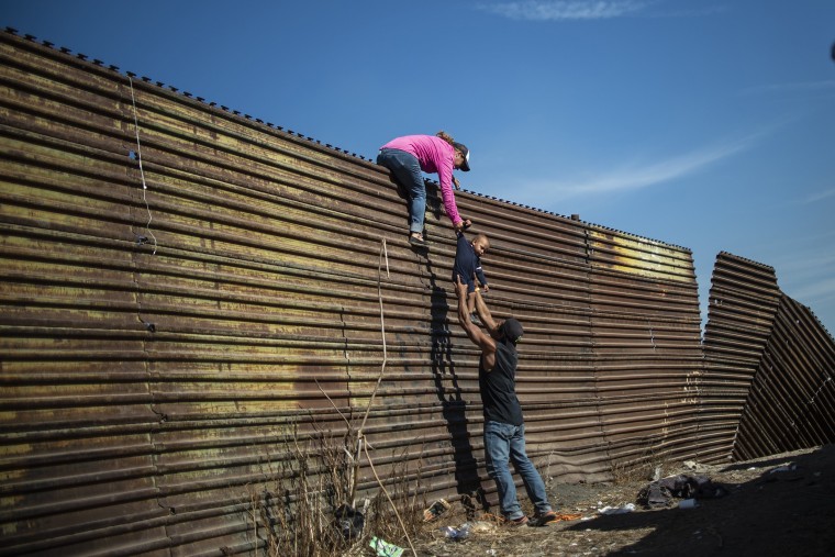 Image: A group of Central American migrants climb the border fence between Mexico and the United States near El Chaparral border crossing in Tijuana