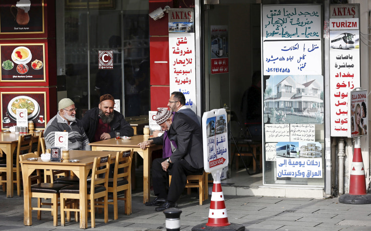 Image: Men chat in front of a real estate agency in Istanbul which has Arabic notices on its window