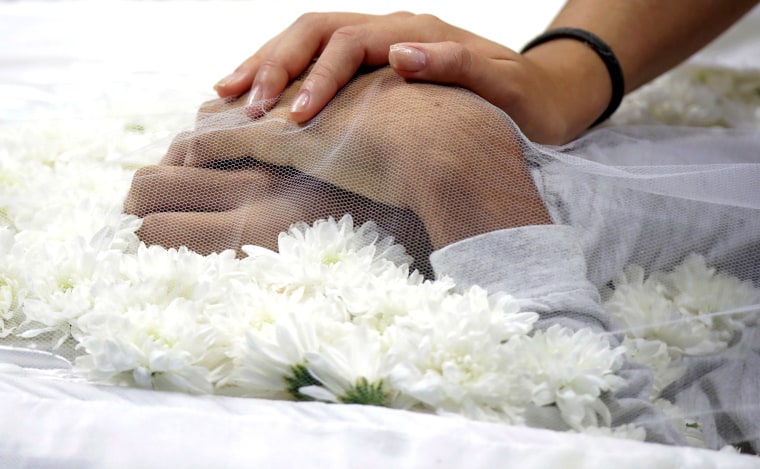 Image: A mourner touches the hand of one of the victims killed in a shooting at Raul Brasil School, during the collective funeral in Suzano