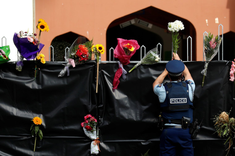 Image: A police officer places flowers at the entrance of Masjid Al Noor mosque in Christchurch