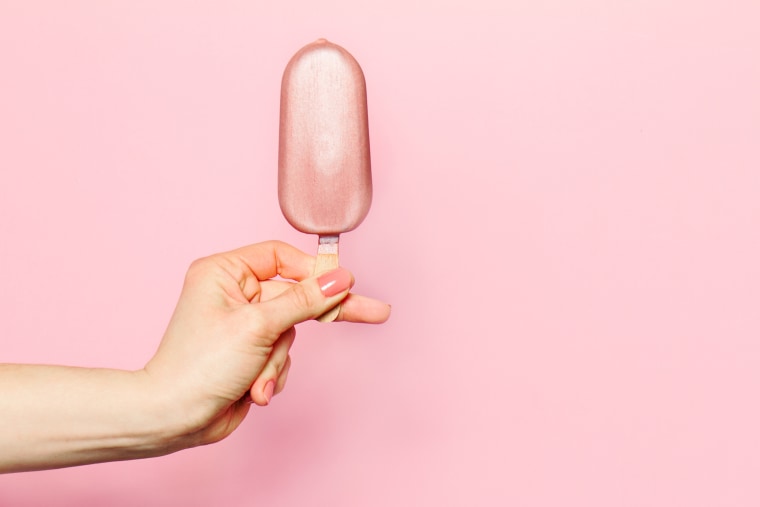 Hand of young woman holding ice cream on pink background.