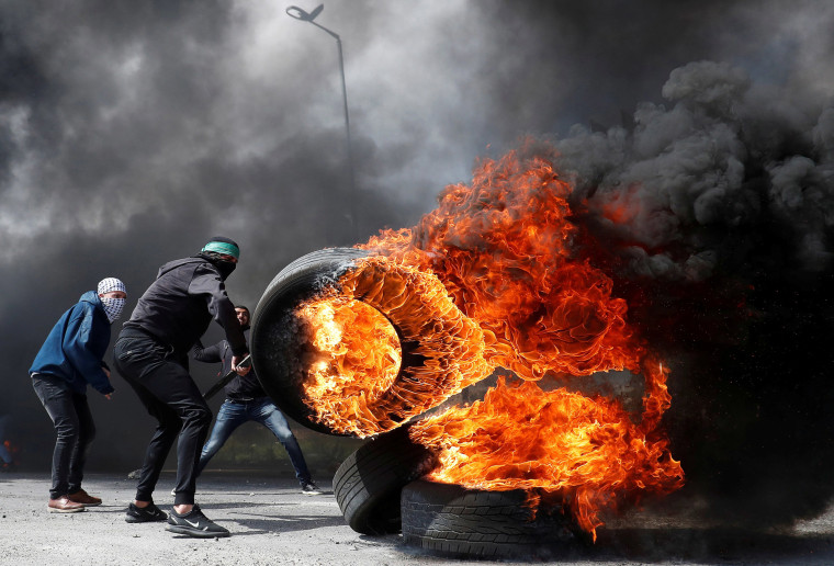 Image: A Palestinian protester moves a burning tire during clashes with Israeli troops in the West Bank