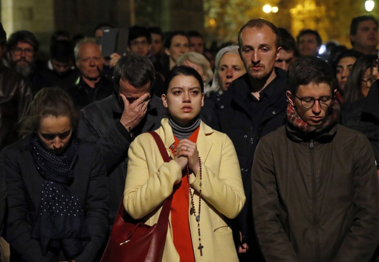 Image: People pray as the Notre Dame cathedral burns in Paris on April 15, 2019.