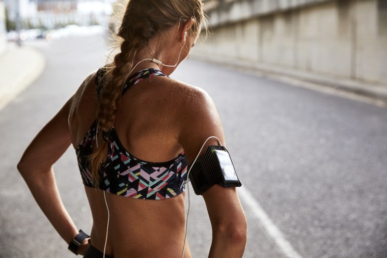Fit female runner in sports bra with mp3 player armband and headphones resting on urban street