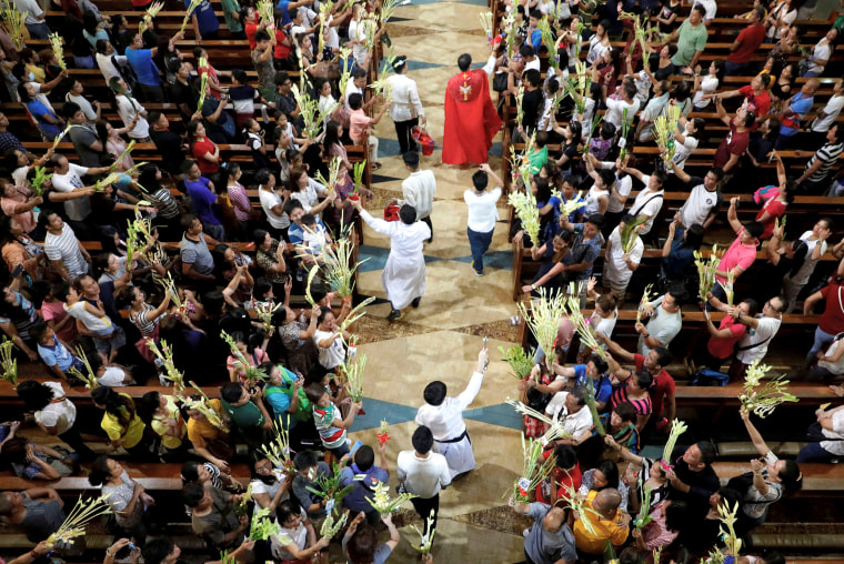 Image: A Catholic priest sprinkles holy water over palm fronds before Palm Sunday mass