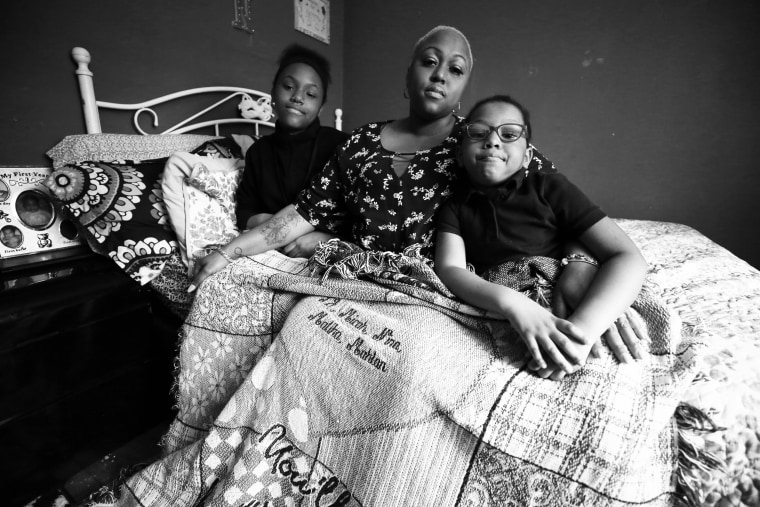 Ashley Gunn sits with her daughters, Nina, left, and Maliha, under a blanket that belonged to her late mother Gwendolyn Fleming, decorated with the names of her five grandchildren.