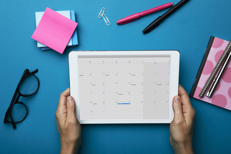 Top view of woman holding tablet with calendar on desk