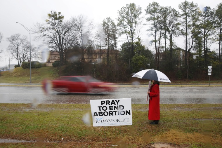Image: Ellie Hermann stands near the street as cars drive by with a protesting sign near the West Alabama Women's Center