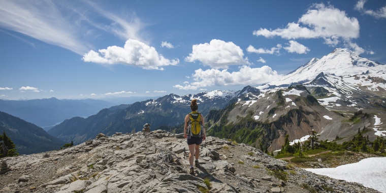 Rear view of female hiker walking on rock formations against mountains and cloudy sky during winter at North Cascades National Park