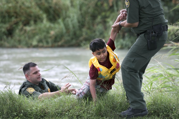 Border Patrol Agent Bryan Kemmett, left, passes a 7-year-old boy from Honduras to another agent after he was rescued from the swollen Rio Grande River on May 10. 