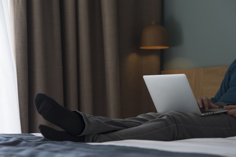 Young man lying on bed using laptop, partial view