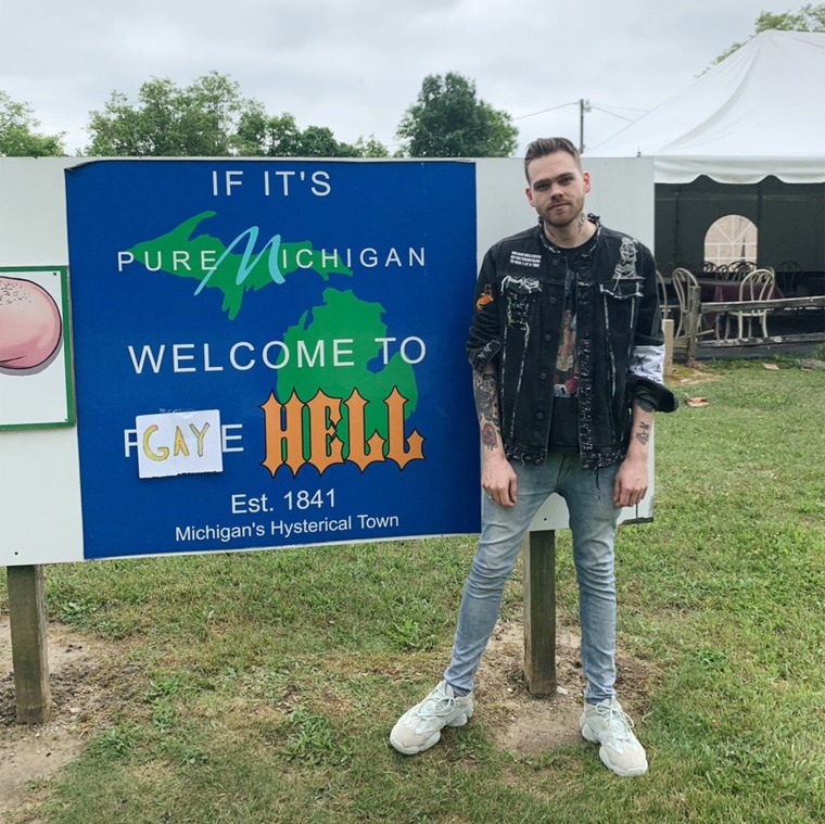 Elijah Daniel stands next to a welcome sign to Gay Hell, Michigan, after he purchased the town. He plans to only fly gay pride flags in honor of LGBTQ Pride Month.