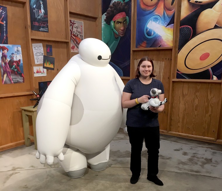 Gillian Burns with her Sony Aibo dog at Disney World, standing with Baymax from the movie "Big Hero 6."