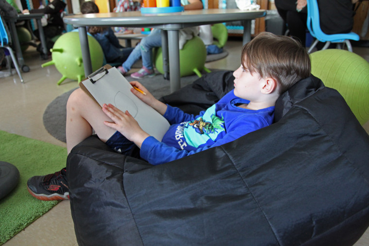Second-grader Jaxson Murchison opts for a bean bag and clip board to complete an art project at Thomas Hooker Elementary School in Meriden, Connecticut.