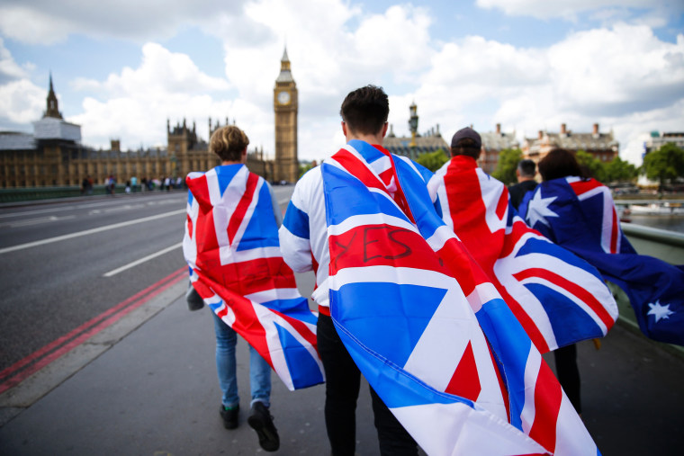 Image: People walk over Westminster Bridge wrapped in Union flags towards the Big Ben and The Houses of Parliament