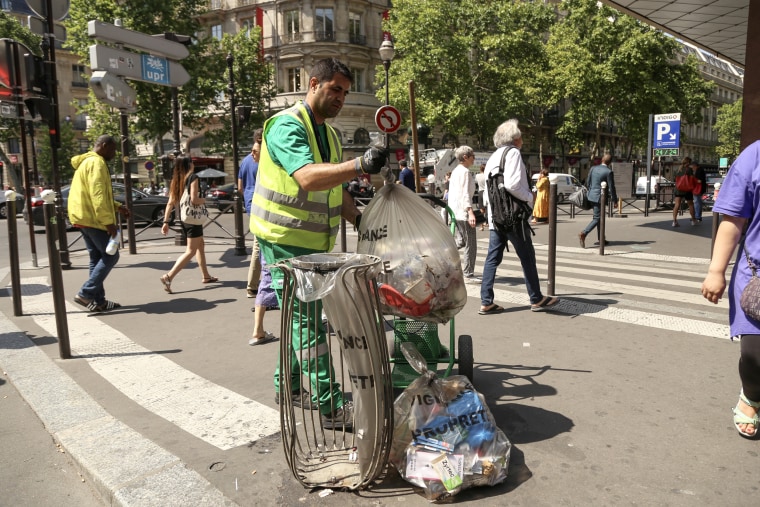 Image: Abdel Hamid tries to stay out of the sun while picking up trash near the popular department store Galaries Lafayette in Paris during a heat wave.