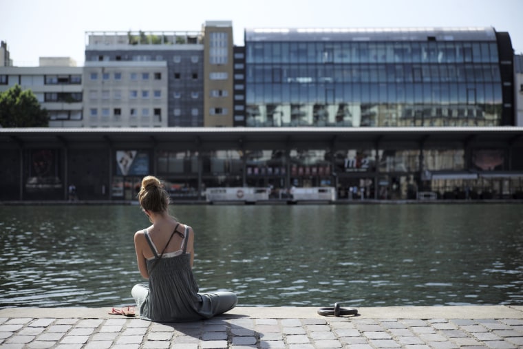 Image: A woman sits under the sun along the Canal de l'Ourcq in Paris,