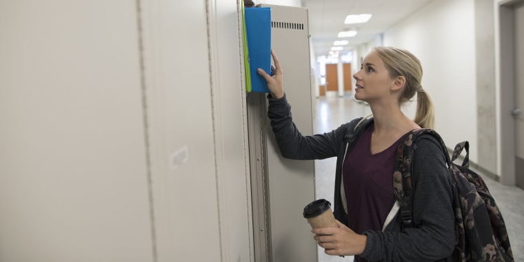 Female high school student removing books from locker in corridor