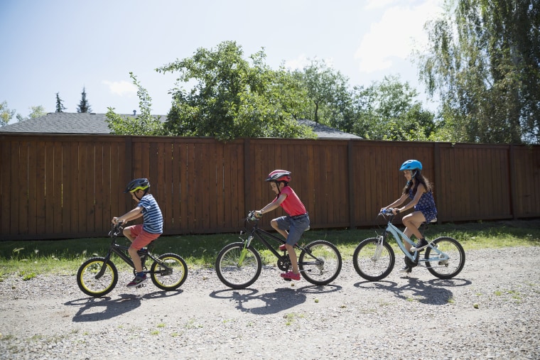 Boys and girl riding bicycles on sunny gravel road in a row