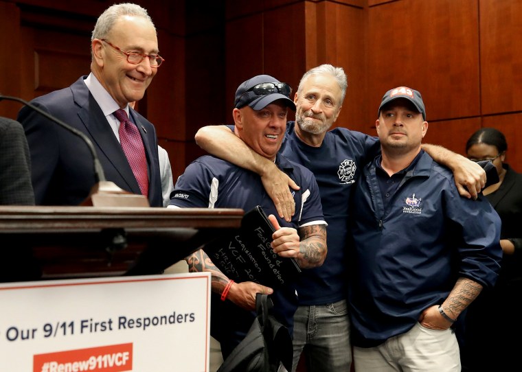 Image: Jon Stewart hugs 9/11 first responders with Sen. Chuck Schumer, D-NY, at a press conference after the Senate voted to renew the September 11th Victim Compensation Fund on July 23, 2019.