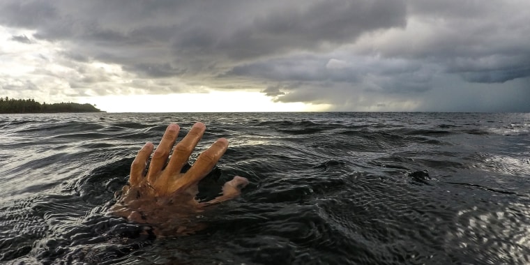 Hand reaching for horizon in the ocean
