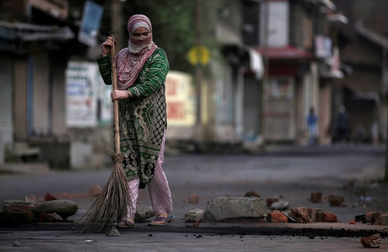 Image: A woman removes pieces of stones and bricks from a road during restrictions after the government scrapped special status for Kashmir, in Srinagar