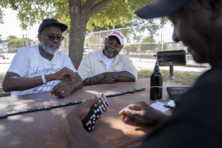 Larry Sanders (R) plays a competitive game of Dominoes with friends René Hopkins (L) and Don Ware or "Don D" before work in Green Meadows Park, Los Angeles on July 25, 2019.