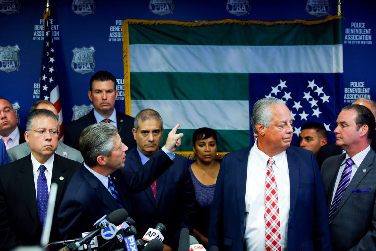 Image: NYPD Police Benevolent Association President Lynch points to the NYPD flag which is hanging upside down as a protest at a news conference in New York