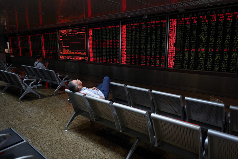 Image: An investor rests on a chair in front of screens showing stock market movements at a securities company in Beijing