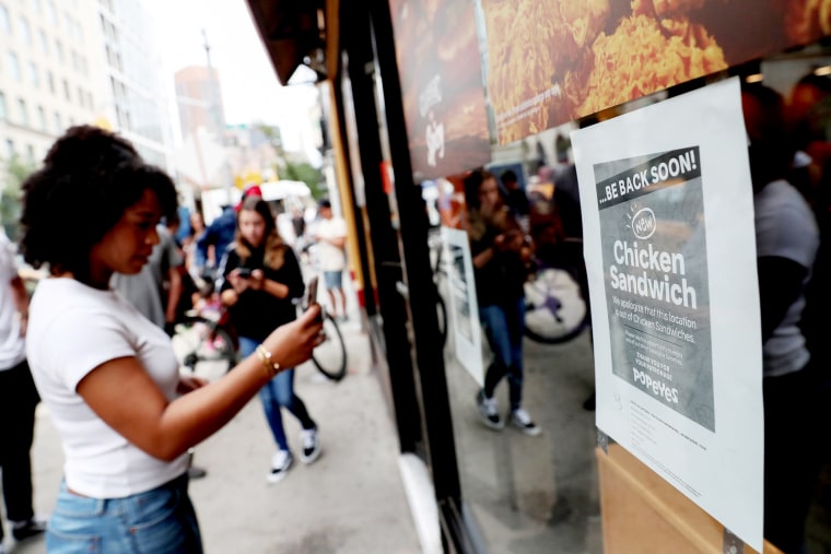 Image: A woman takes a picture of a sign posted outside Popeyes Louisiana Kitchen stating that the restaurant is out of their new chicken sandwiches in New York