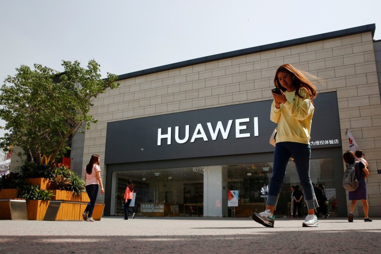 Image: FILE PHOTO: A woman looks at her phone as she walks past a Huawei shop in Beijing