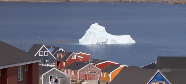 An iceberg floats past a village in Greenland.